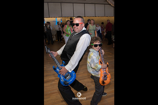 Wedding guests playing air guitar on dance floor by Susan Knott Photography